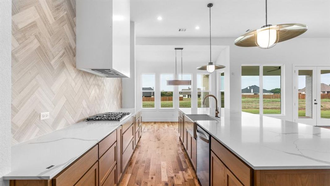 Kitchen featuring light wood-type flooring, light stone counters, sink, hanging light fixtures, and stainless steel appliances