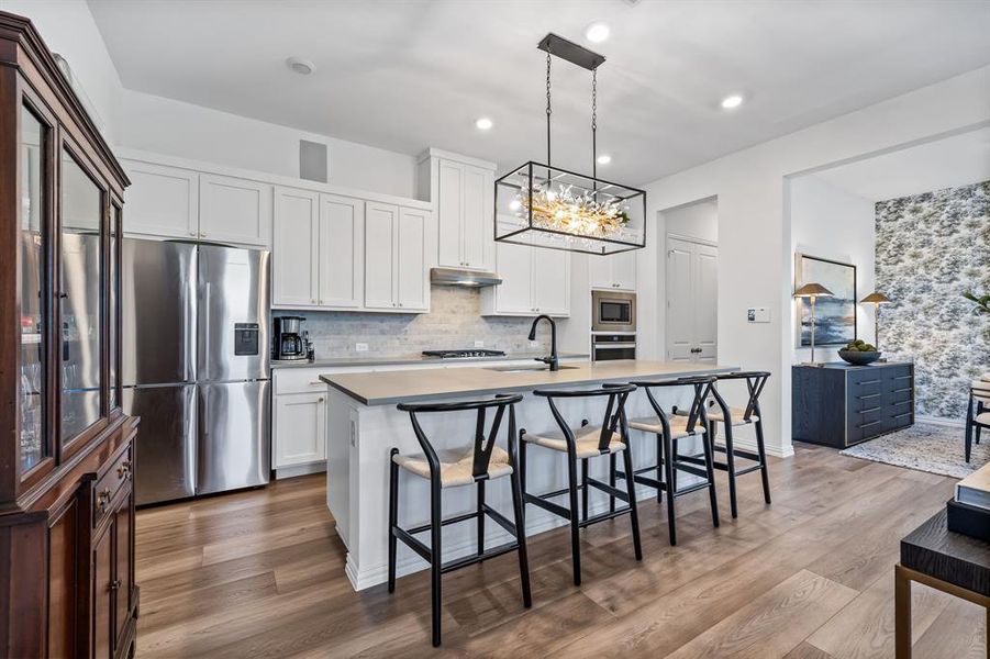 Kitchen with appliances with stainless steel finishes, a kitchen island with sink, wood-type flooring, and white cabinets