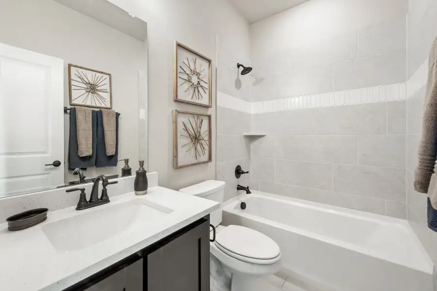 Bathroom with white quartz vanity, dark cabinets, and tiled shower-tub combo with matte black fixtures Bathroom with white quartz vanity, dark cabinets, and tiled shower-tub combo with matte black fixtures