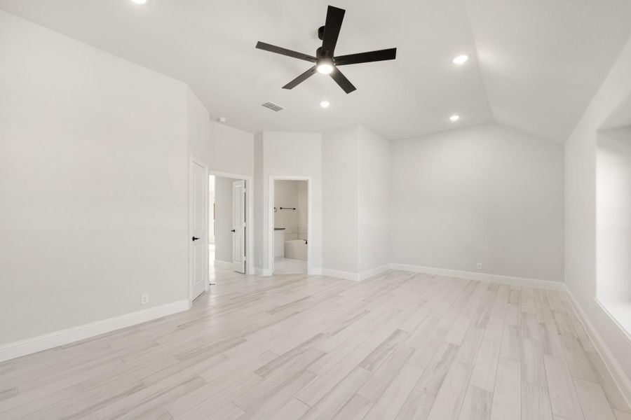 Empty master bedroom with light wood floors, black ceiling fan, and ensuite bathroom doorway