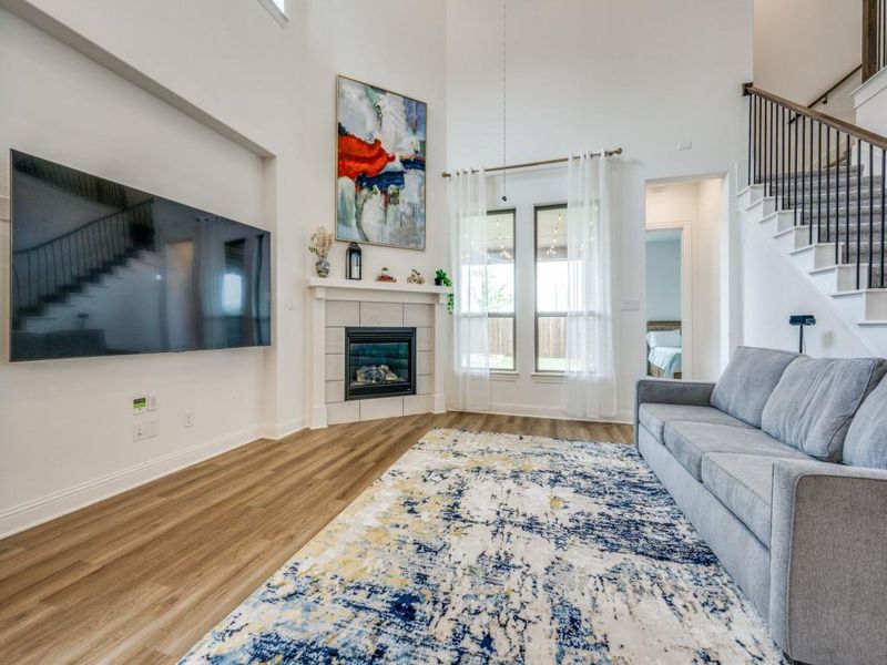 Living room with stairs, baseboards, a towering ceiling, a fireplace, and wood finished floors