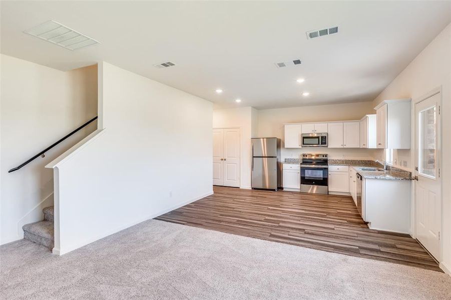 Kitchen with appliances with stainless steel finishes, white cabinets, dark colored carpet, and recessed lighting