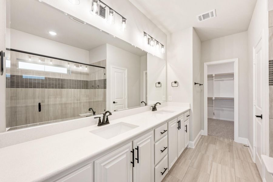 Master bathroom with double vanity, white cabinets, walk-in shower, and doorway to closet