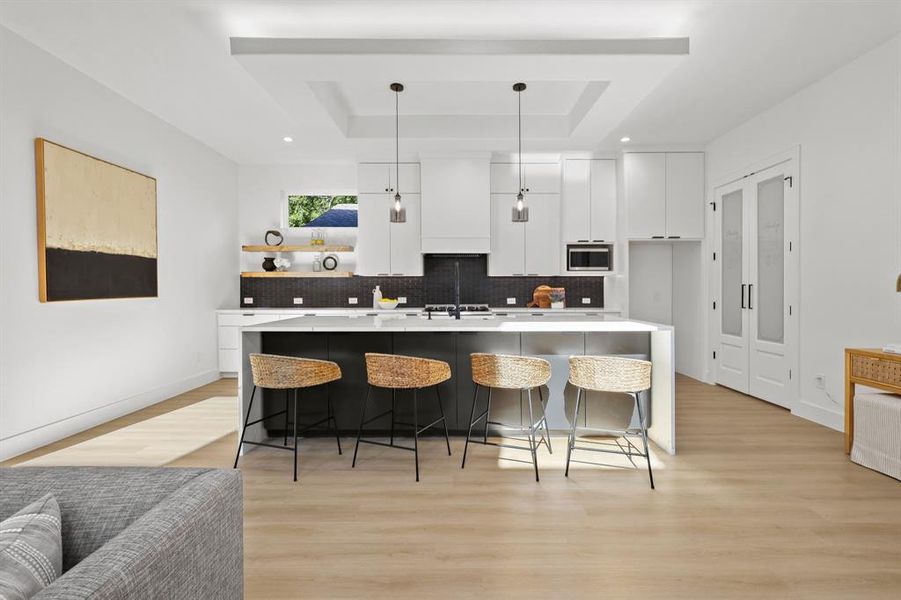 Kitchen featuring light wood-type flooring, stainless steel microwave, a tray ceiling, and white cabinetry