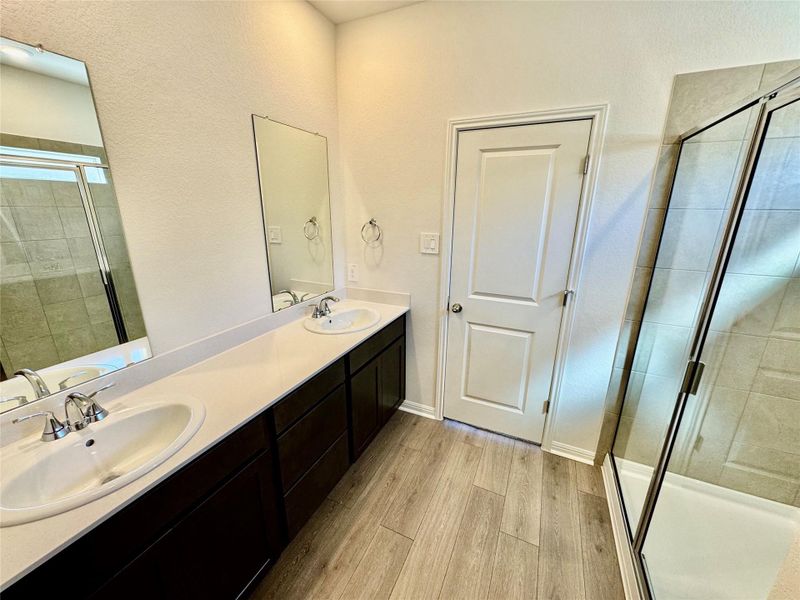 Bathroom with a shower stall, light wood-style floors, double vanity, and a textured wall Bathroom with a shower stall, light wood-style floors, double vanity, and a textured wall