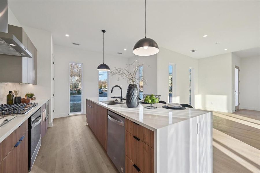 Kitchen with a spacious island, sink, stainless steel appliances, light hardwood / wood-style floors, and wall chimney range hood