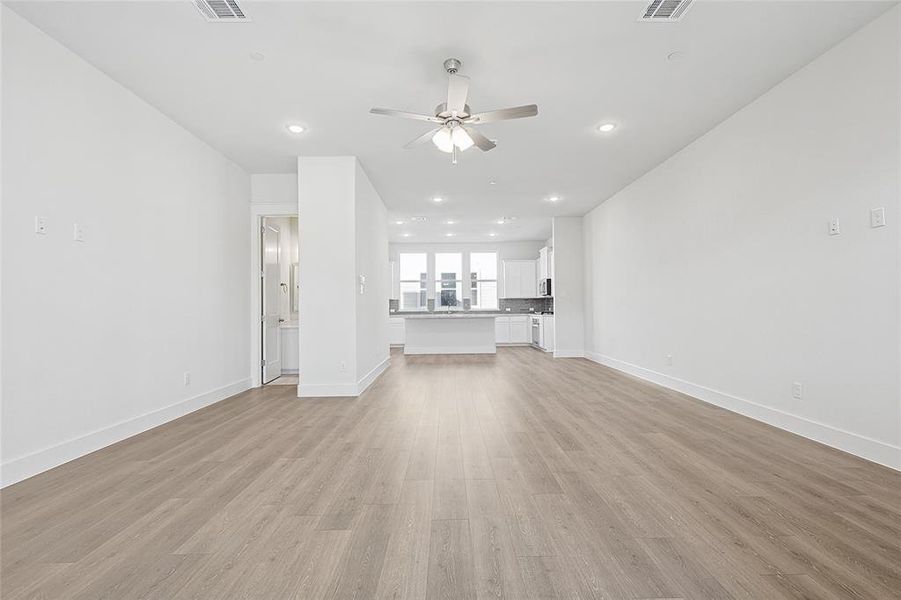 Spacious living area featuring light-toned flooring, white walls, recessed lighting, and a ceiling fan
