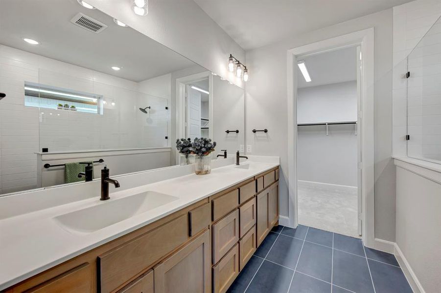 Full bathroom featuring a walk in shower, double vanity, a spacious closet, and dark tile patterned floors