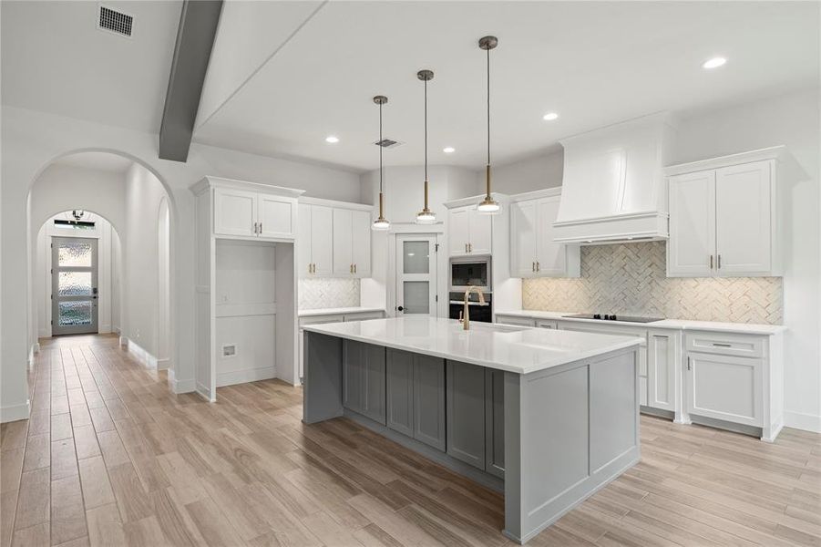 Kitchen featuring arched walkways, white cabinetry, beamed ceiling, light wood-style floors, and recessed lighting