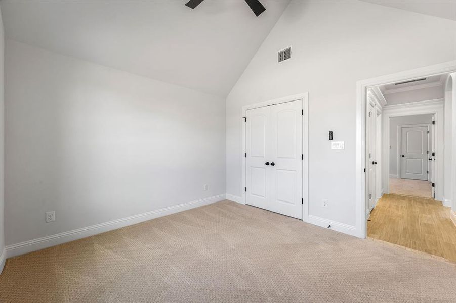 Unfurnished bedroom with ceiling fan, light colored carpet, a closet, and high vaulted ceiling