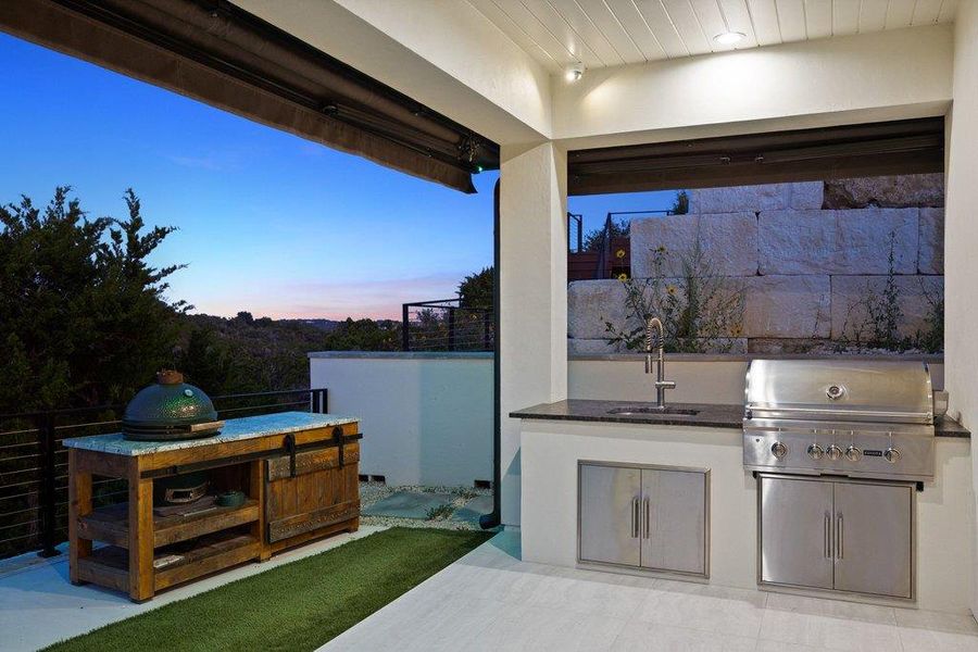 An outdoor kitchen, complete with a built-in grill and sink, offers picturesque views of the surrounding landscape.