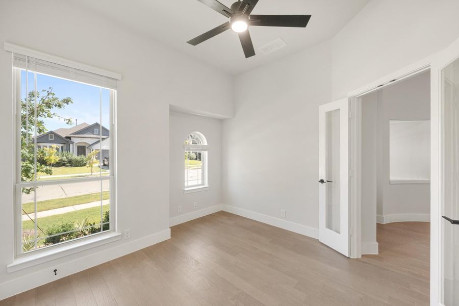 Empty bedroom with light wood floors, ceiling fan, large windows, and arched accent window