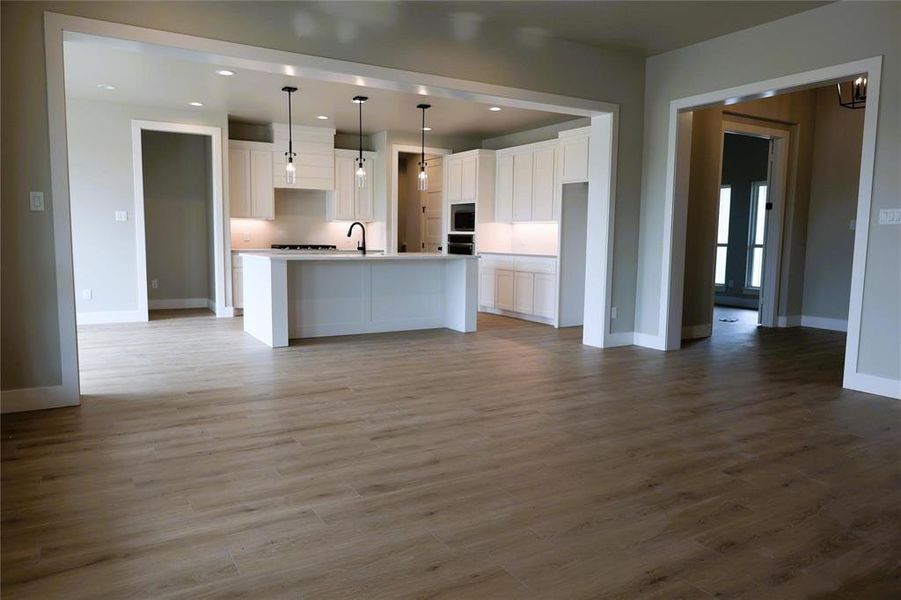 Kitchen with pendant lighting, white cabinets, a center island with sink, and hardwood / wood-style floors