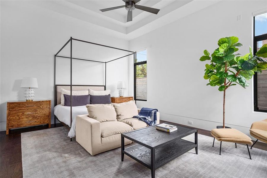 This serene first-floor primary suite offers a luxurious retreat with its spacious layout, tray ceiling, and large windows that bring in abundant natural light.