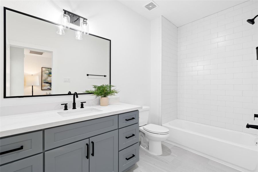 Designed with a contemporary aesthetic, this bathroom features a stylish gray vanity with black hardware and a crisp white quartz countertop.