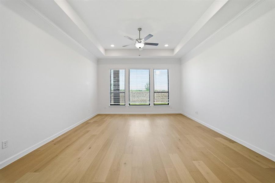 Spacious room featuring light wood-finish flooring and a tray ceiling with recessed lighting Spacious room featuring light wood-finish flooring and a tray ceiling with recessed lighting