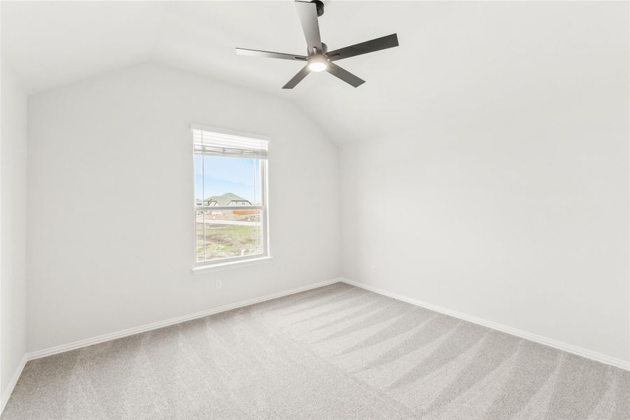 Empty bedroom with vaulted ceiling, ceiling fan, carpet flooring, and single window with outdoor view Empty bedroom with vaulted ceiling, ceiling fan, carpet flooring, and single window with outdoor view