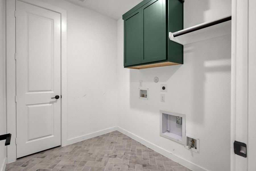 The laundry room features tile flooring laid in a diagonal brick pattern. There are painted cabinets in the space plus room for a refrigerator.