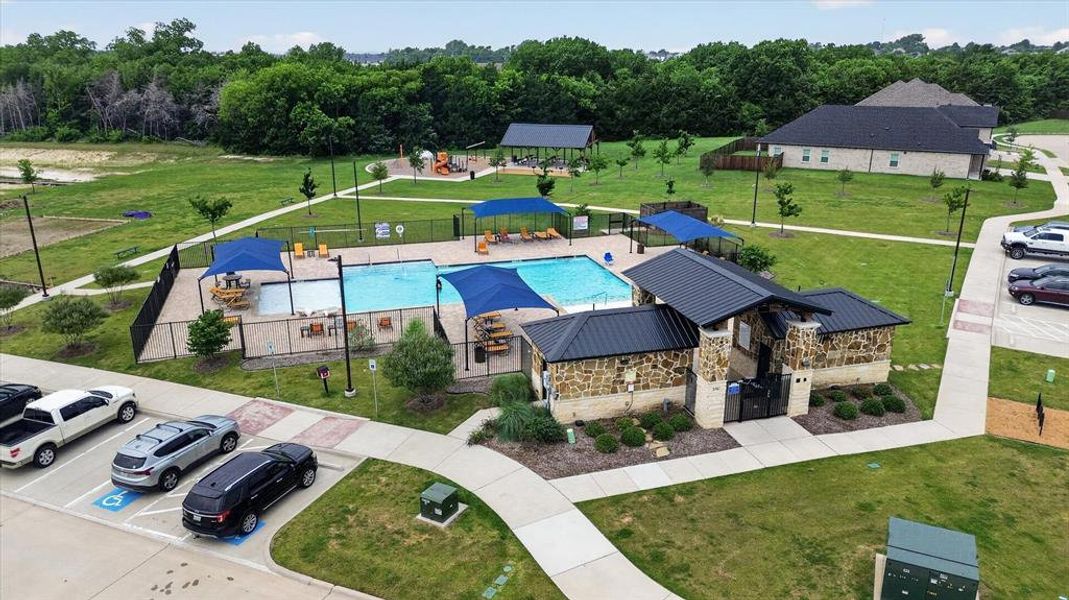 Community amenities featuring a swimming pool, shaded seating areas, a stone-clad building with a dark metal roof, and an adjacent playground