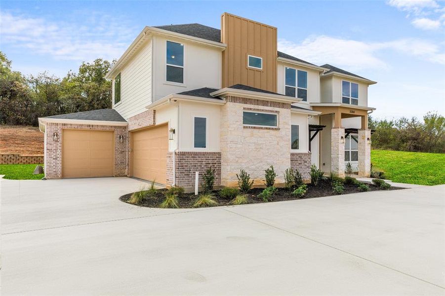View of front facade with board and batten siding, driveway, stone siding, an attached garage, and roof with shingles
