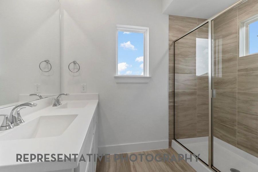 The primary bathroom features dual sinks with ample cabinetry, a window for natural light, and a spacious shower, combining functionality with comfort and style.