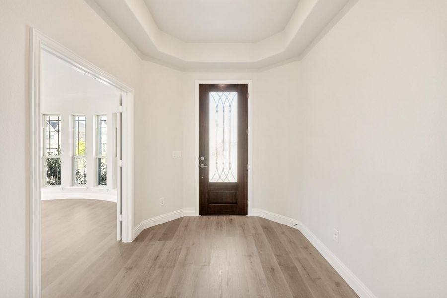 Entryway with dark wood front door, decorative glass panel, tray ceiling, and light hardwood floors Entryway with dark wood front door, decorative glass panel, tray ceiling, and light hardwood floors