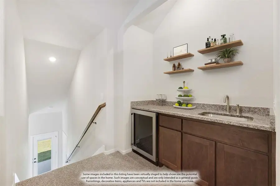 Wet bar with dark wood cabinets, granite countertop, sink, wine fridge, and floating shelves near carpeted staircase landing