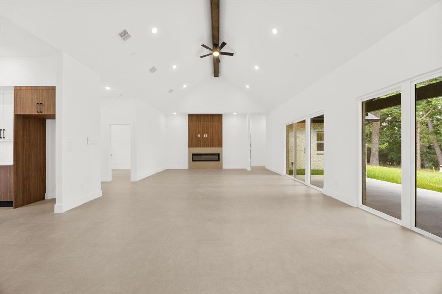 Spacious living room with vaulted ceilings, exposed beam, and sleek electric fireplace.