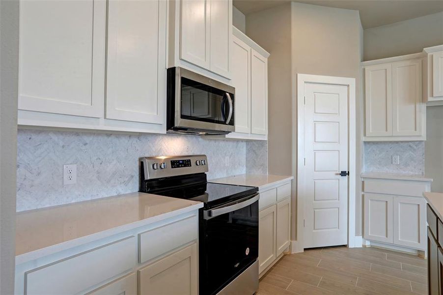 Kitchen with tasteful backsplash, stainless steel appliances, white cabinets, and light wood-type flooring