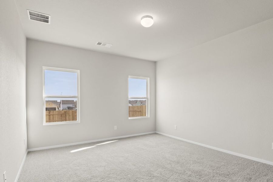 Image of a primary bedroom with light grey walls, two windows, and tan carpeting