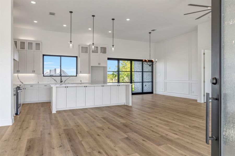 Kitchen featuring glass insert cabinets, a kitchen island, open floor plan, hanging light fixtures, and white cabinets