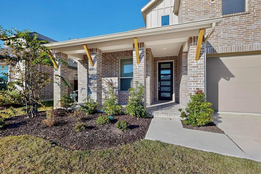 Entrance to property featuring a porch, a garage, brick siding, and board and batten siding Entrance to property featuring a porch, a garage, brick siding, and board and batten siding