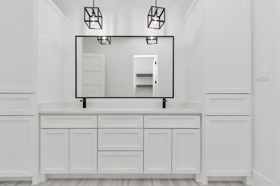 This is a sleek, modern bathroom vanity area featuring clean white cabinetry, a large mirror with a black frame, and chic geometric light fixtures.