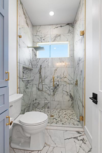 Bathroom with a marble finish shower and marble look tile flooring