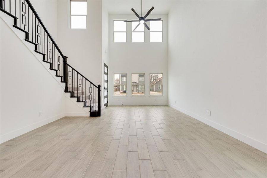 Unfurnished living room with a ceiling fan, light wood-style flooring, baseboards, and stairs