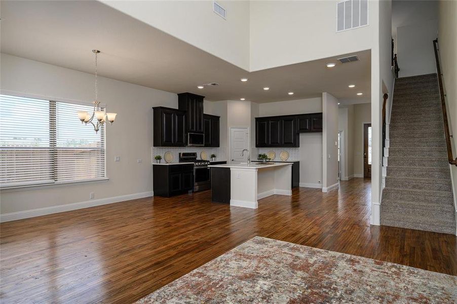 Kitchen featuring stainless steel appliances, hanging light fixtures, dark hardwood / wood-style floors, a center island with sink, and a towering ceiling