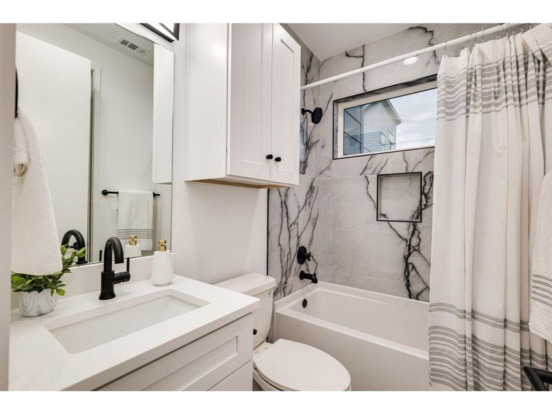 Ensuite bathroom adorned with exquisite marbled tile and featuring a sophisticated shower and tub combo.