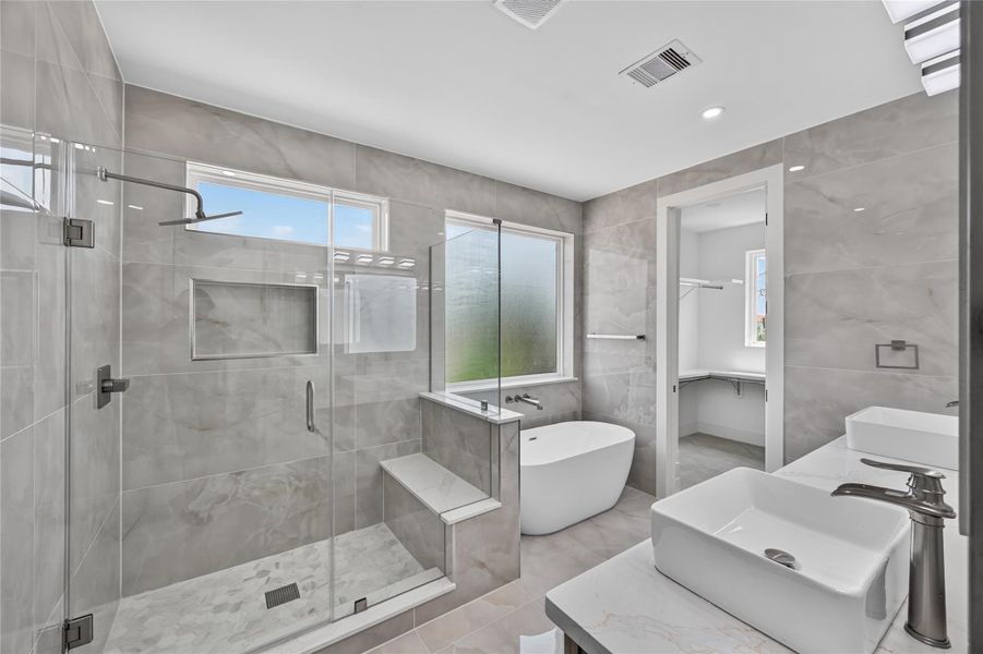 Primary resort style bathroom with frameless glass shower and separate soaking tub, fully tiled with beautiful creamy toned glossy tile.