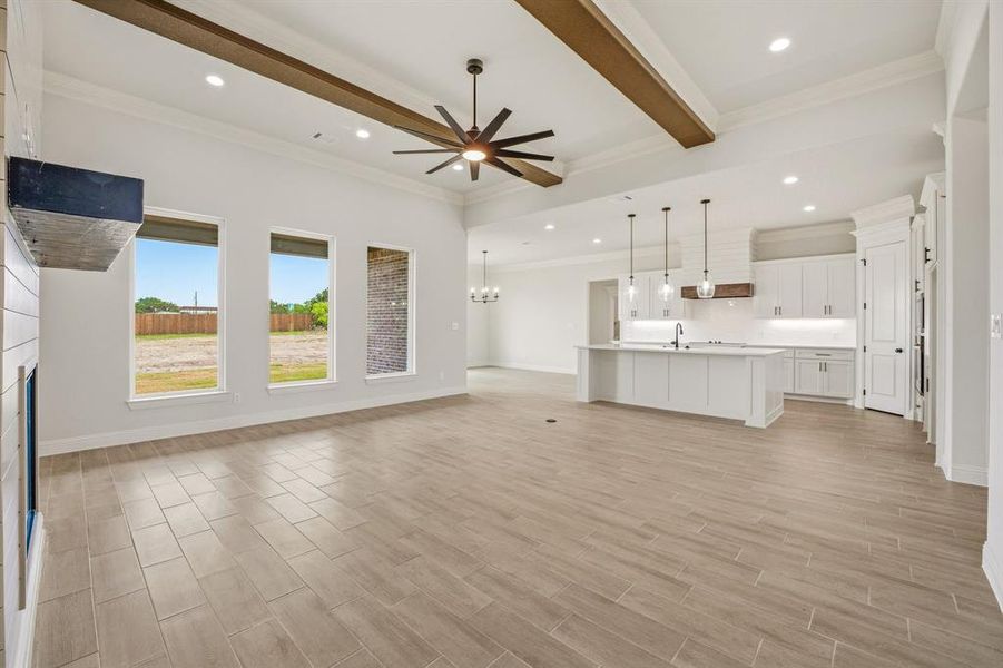 Unfurnished living room featuring ceiling fan, wood finish floors, beam ceiling, ornamental molding, and suspended lighting