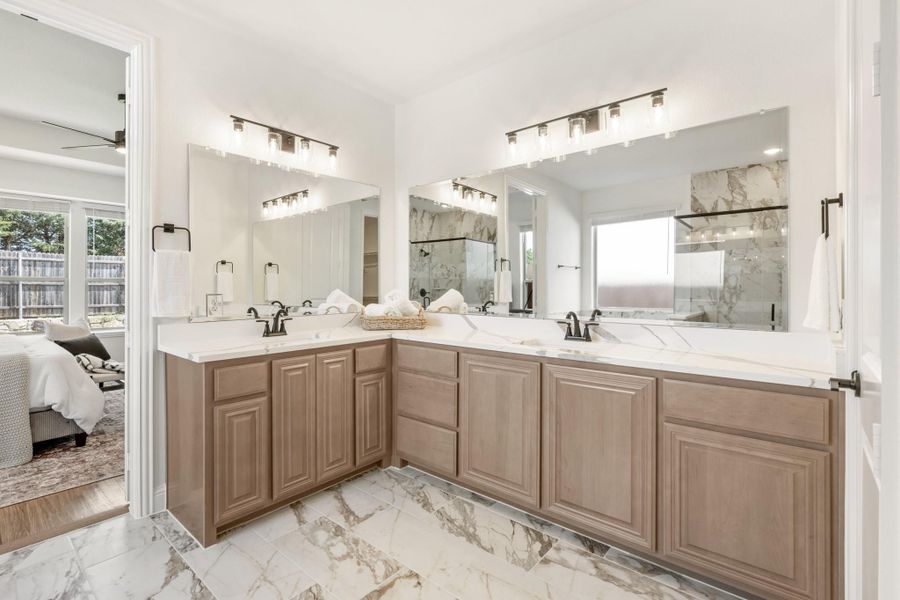Master bathroom with dual vanity sinks, wood cabinets, white countertops, and marble tile floors