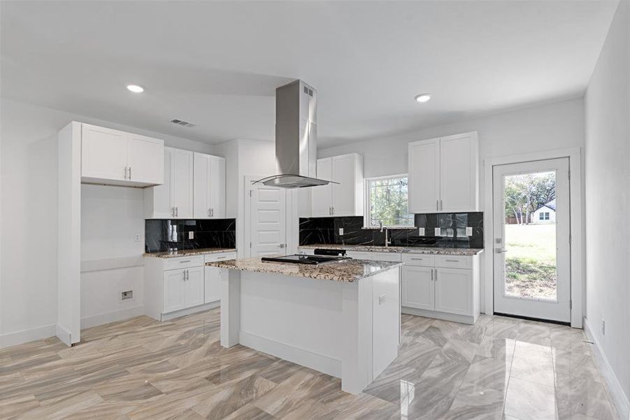 Kitchen featuring decorative backsplash, a kitchen island, light stone countertops, island range hood, and white cabinetry