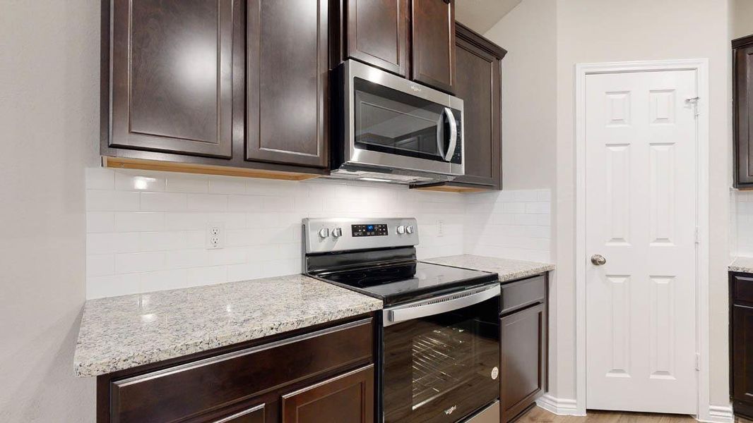 Kitchen with stainless steel appliances, backsplash, dark wood finish cabinets, and light stone counters