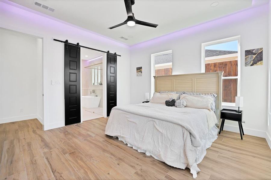 Bedroom featuring a barn door, ceiling fan, ensuite bathroom, and light hardwood / wood-style floors