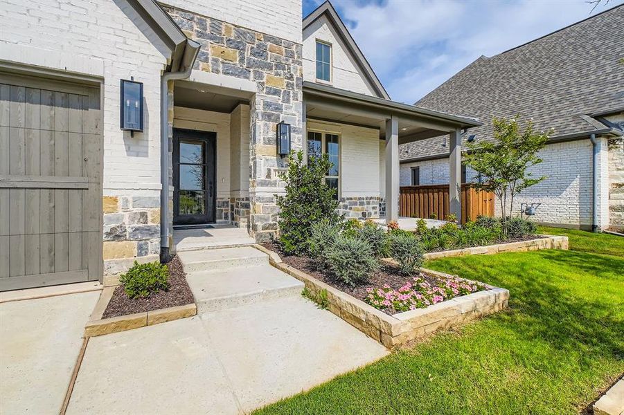 Property entrance with covered porch, stone siding, and a lawn Property entrance with covered porch, stone siding, and a lawn