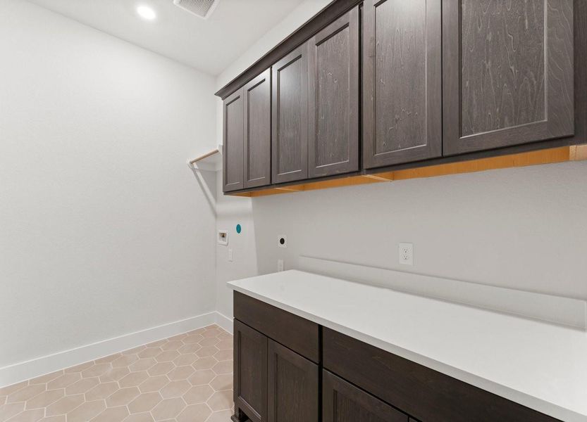 The bright laundry room features dark wood cabinetry offering ample storage space. It features a sleek countertop and a tiled floor, providing a clean and functional area for laundry tasks.