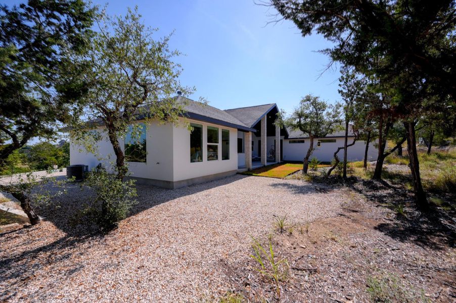 Mature trees frame a modern single-story residence featuring clean white stucco and integrated stone accents.