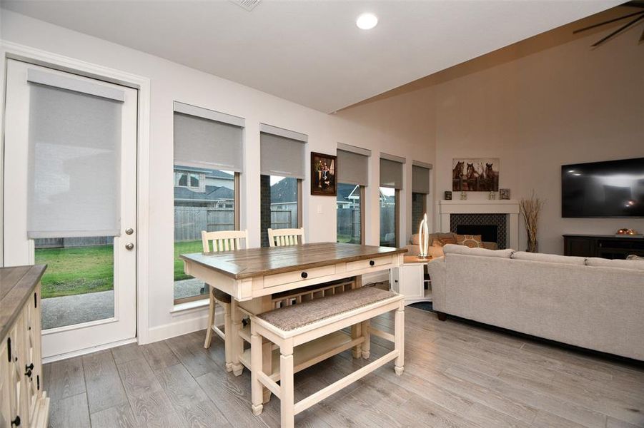 This inviting living area features an open layout with a cozy fireplace, ample natural light from large windows, and elegant wood flooring. The space includes a breakfast area, perfect for gatherings.