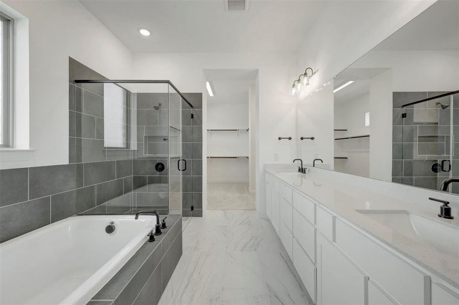 Spacious bathroom featuring a built-in soaking tub with dark-toned tile surround, a glass-enclosed shower with contrasting tile, and a double vanity with an integrated countertop and undermount sinks Spacious bathroom featuring a built-in soaking tub with dark-toned tile surround, a glass-enclosed shower with contrasting tile, and a double vanity with an integrated countertop and undermount sinks