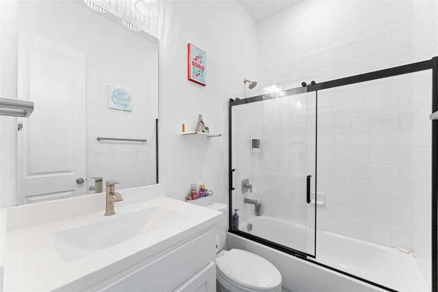 Bathroom featuring a vanity with a white countertop and an integrated sink, a large mirror, and a bathtub with a black-framed glass sliding door