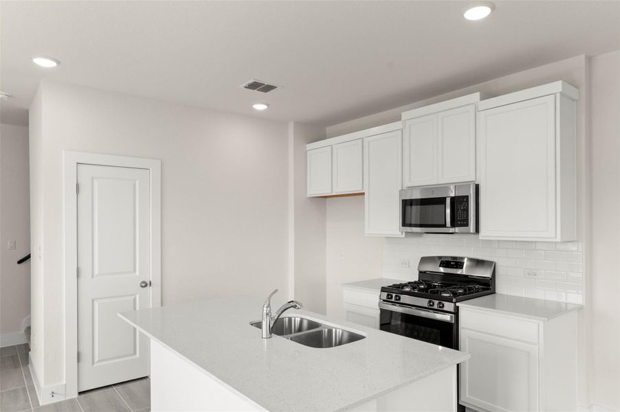 Kitchen featuring decorative backsplash, a center island with sink, white cabinetry, a sink, and stainless steel appliances